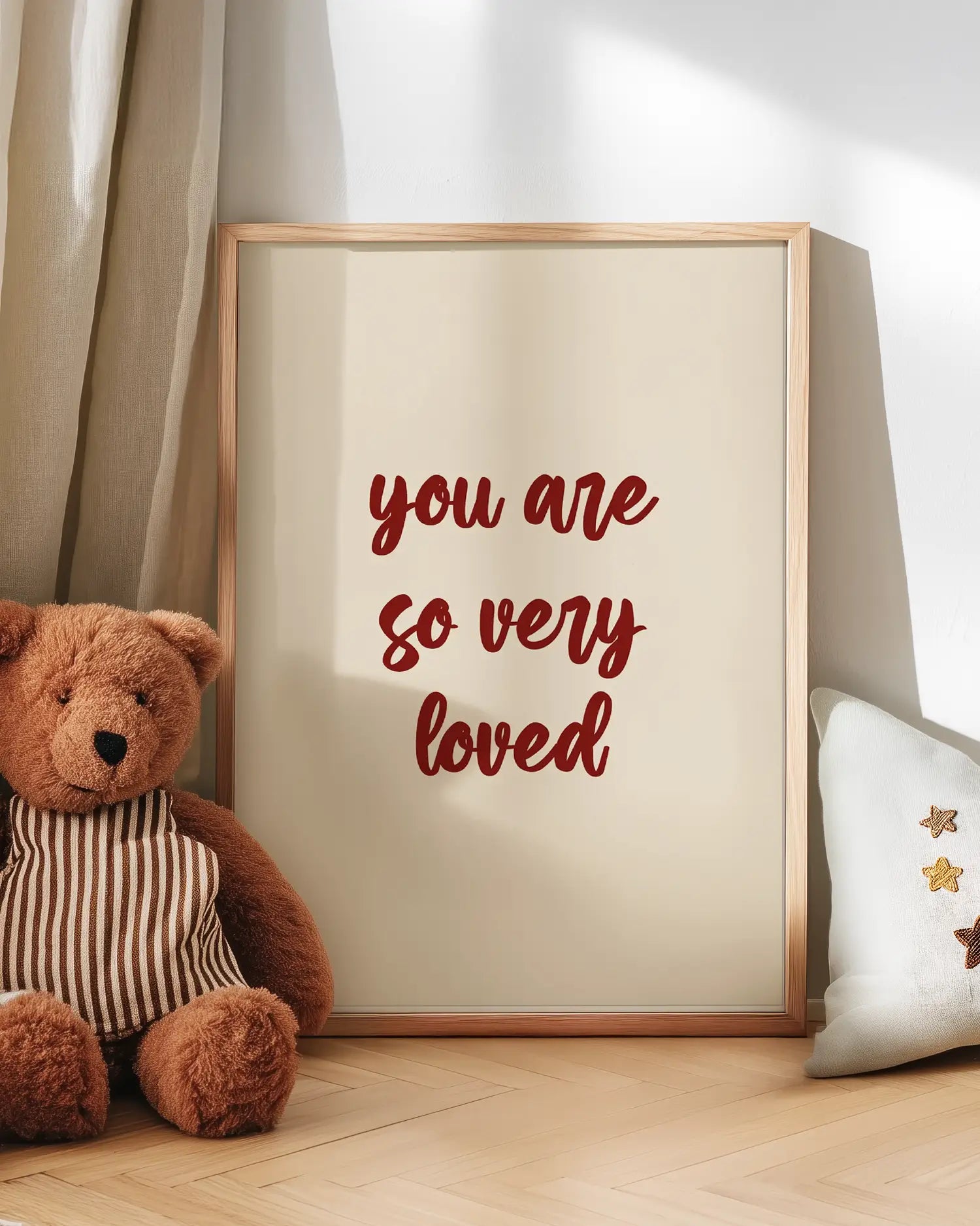 Artwork with 'you are so very loved' text next to a teddy bear on a wooden floor.
