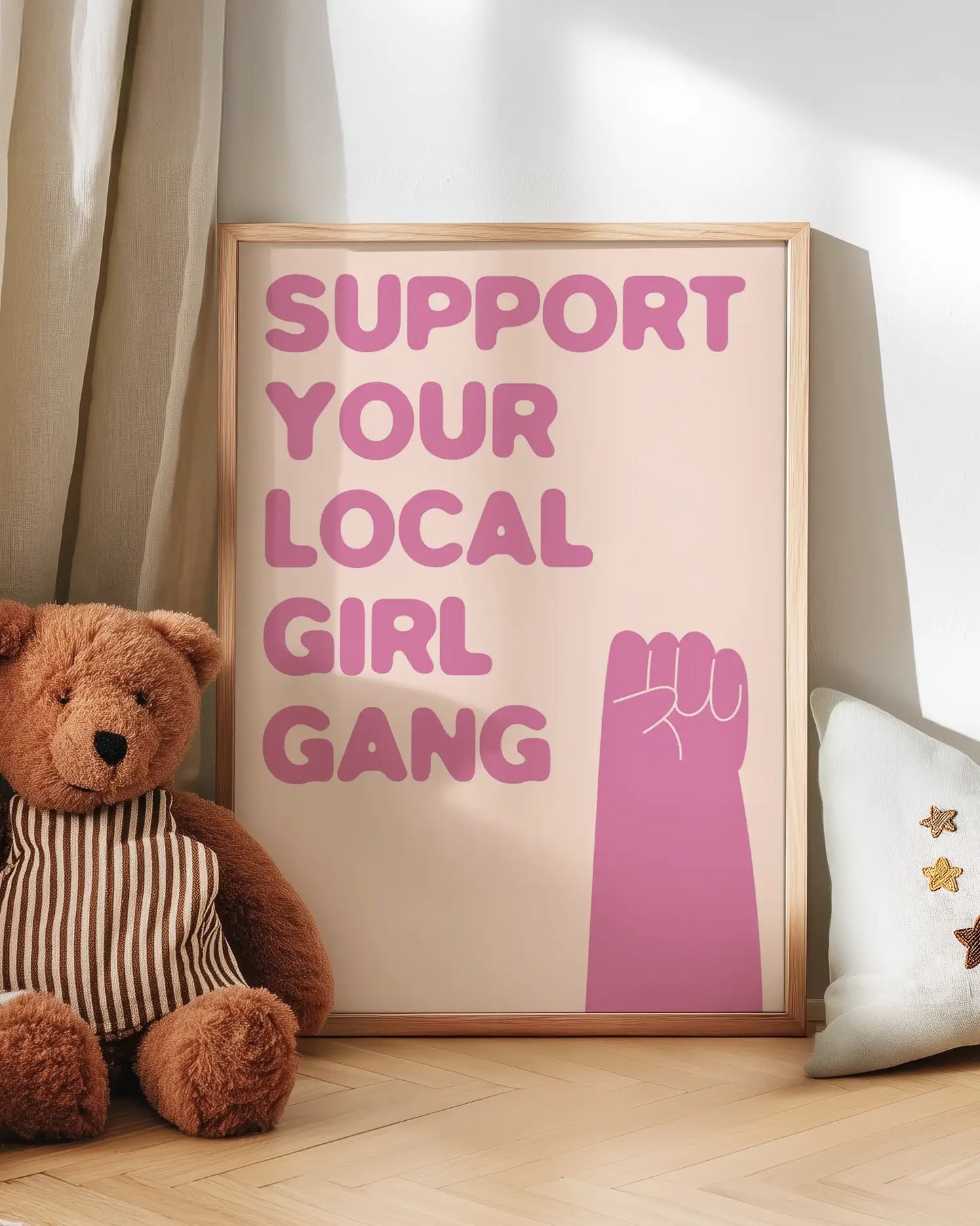 Poster with 'Support Your Local Girl Gang' text and a pink fist graphic, next to a teddy bear and decorative pillow.