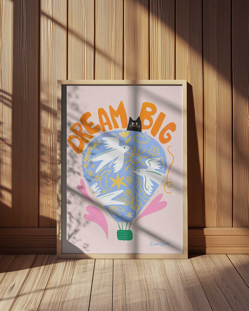 Nursery poster of a hot air ballon and the text 'Dream big' written on it. Framed and leaning against a wooden wall.